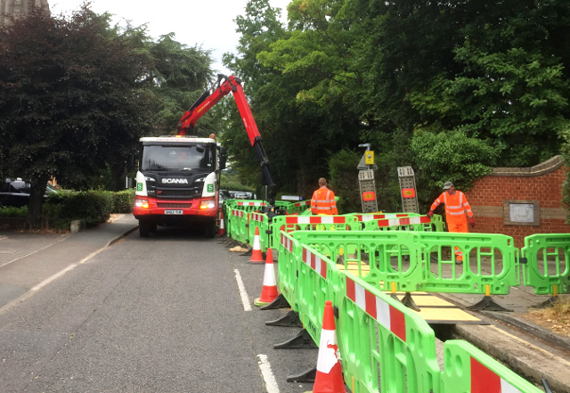 green plastic barriers blocking off the right hand side of a tree-lined road with a lorry with grabber extended blocking the other half.