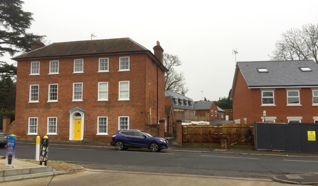 a large red brick residence with 3 storeys and 14 windows visible from the front, a new brick building to its left and further new houses visible in the distance between them